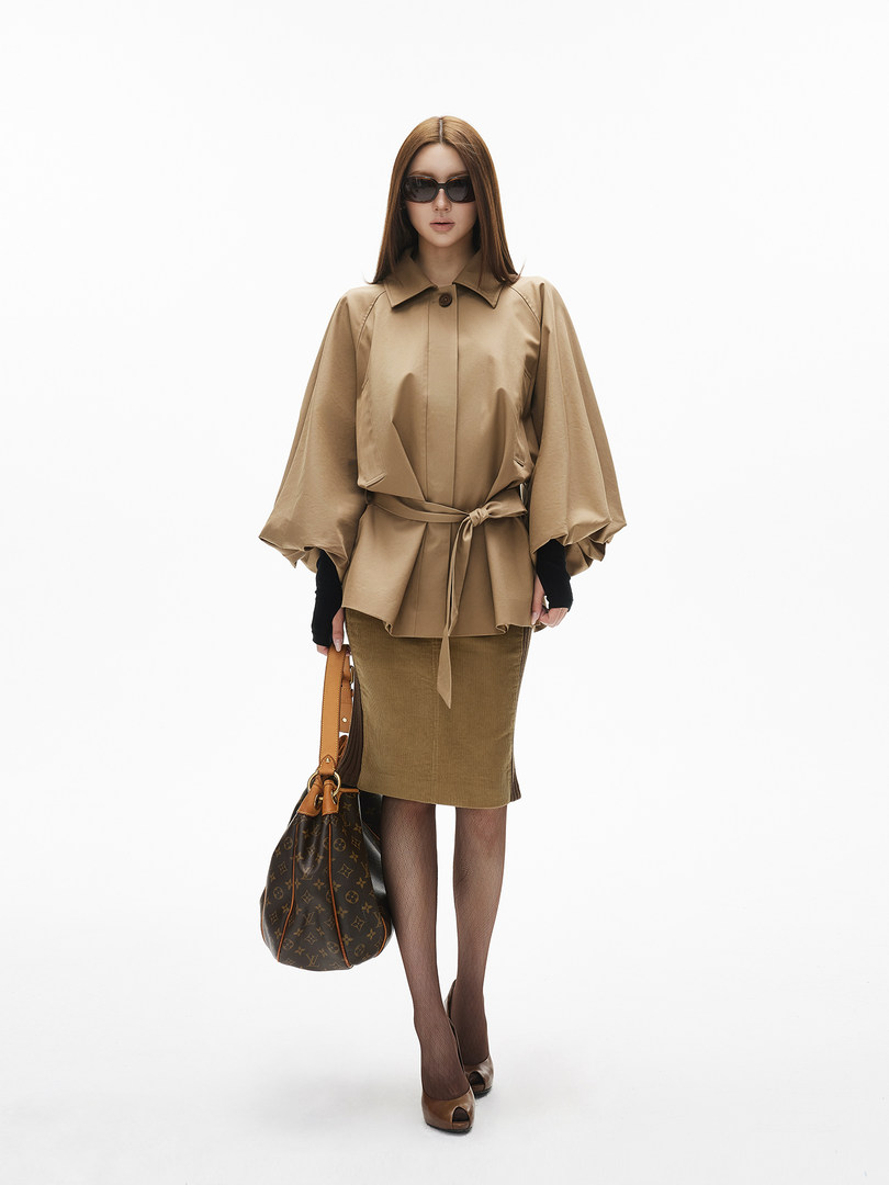 Model wearing a tan belted blouse with matching skirt and handbag
