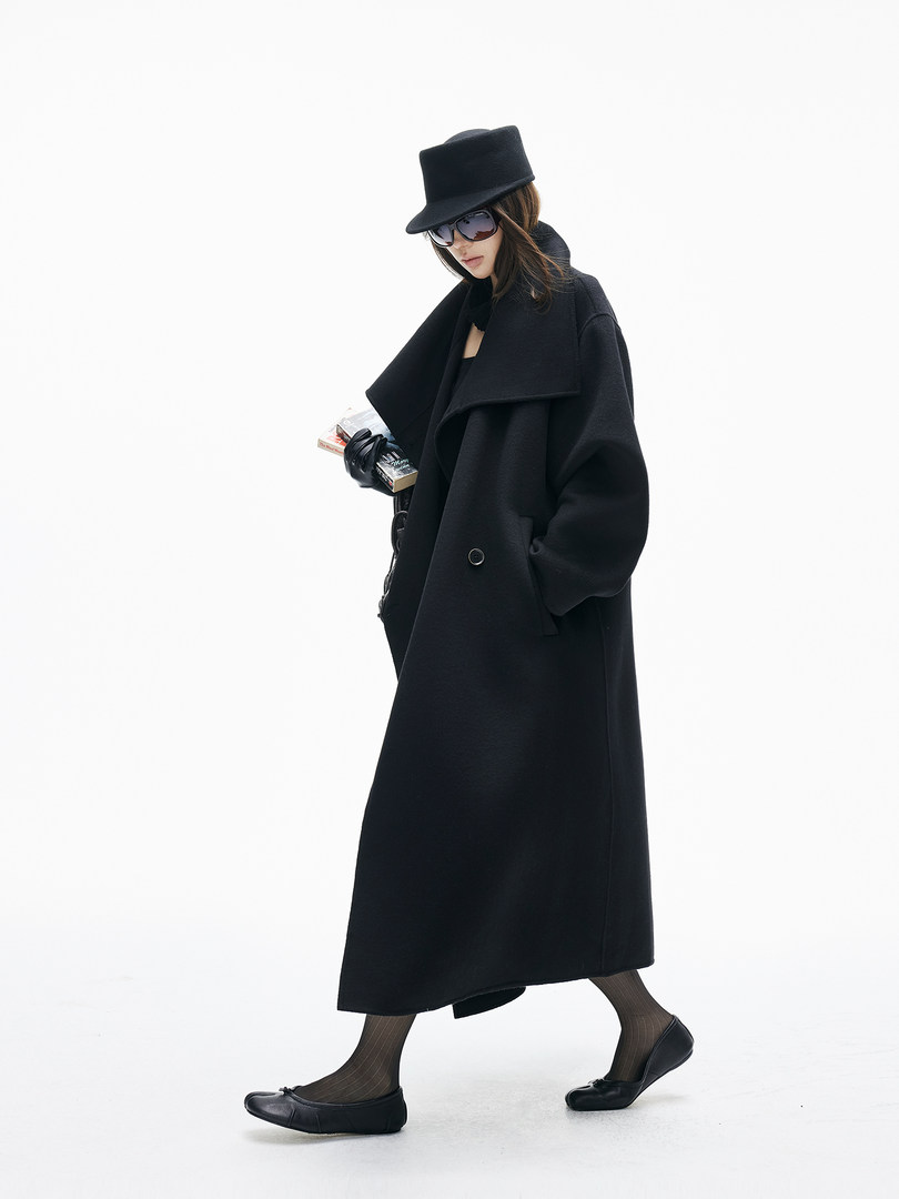 Model wearing a long black oversized coat with black hat and shoes