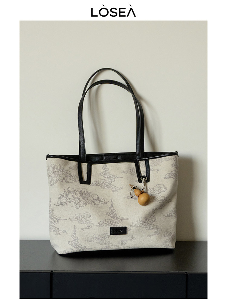 Beige patterned tote handbag with black handles and charm