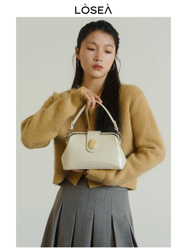 Model holding a cream handbag with a rounded flap detail