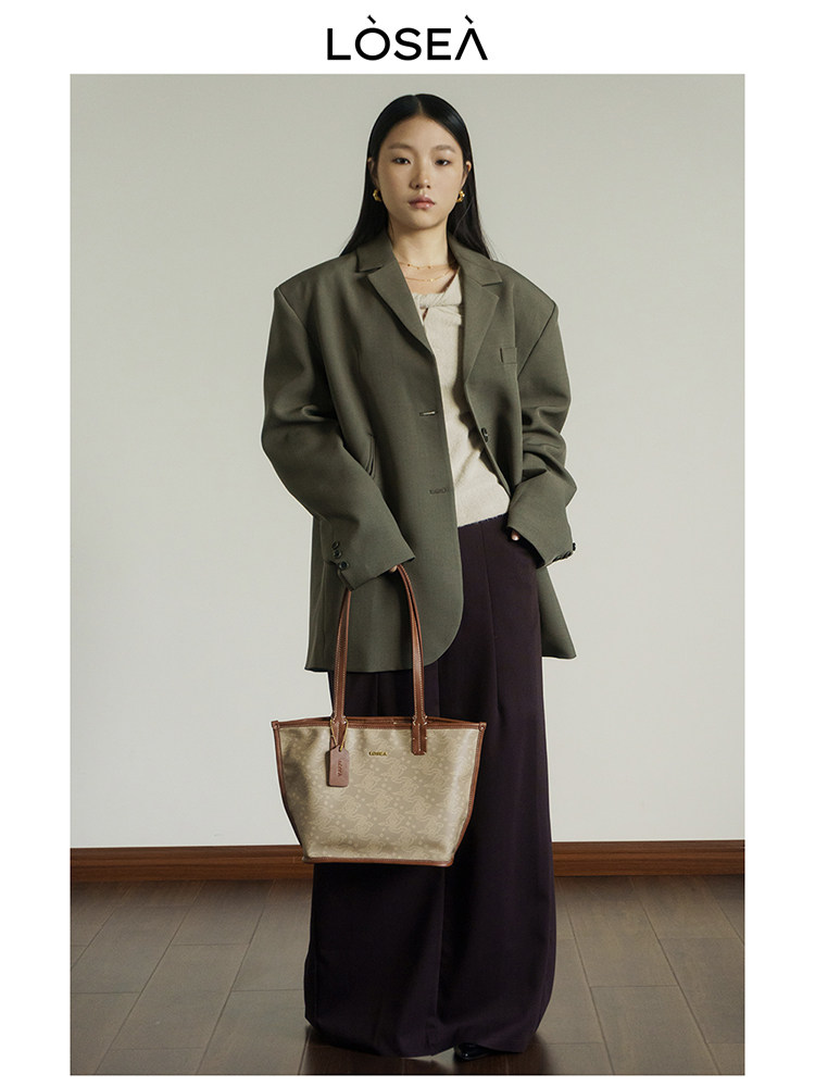Model wearing an oversized olive blazer and carrying a beige tote bag