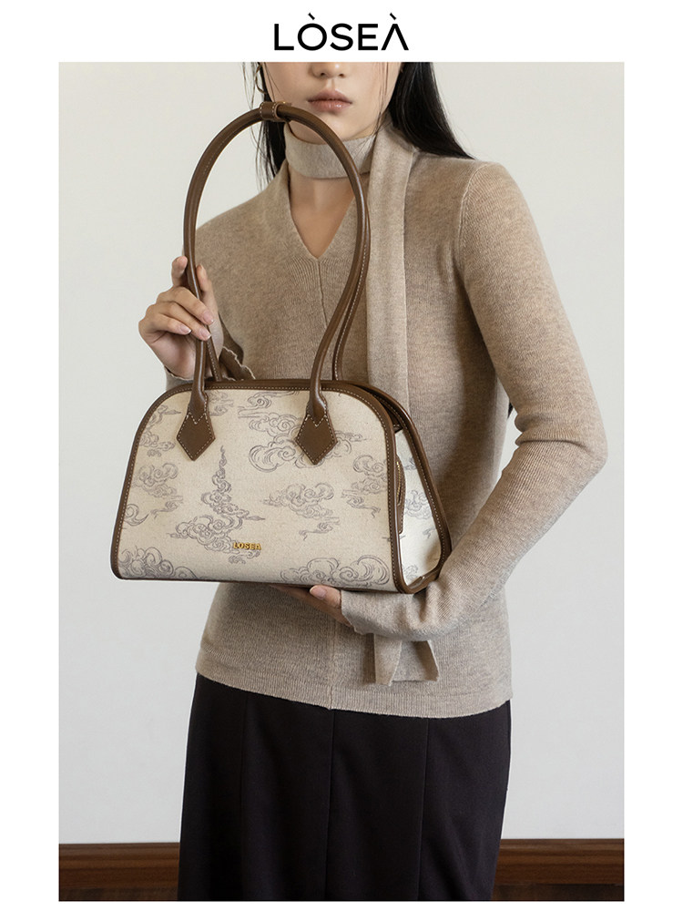 Beige patterned shoulder handbag held by a model