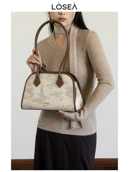 Beige patterned shoulder handbag held by a model