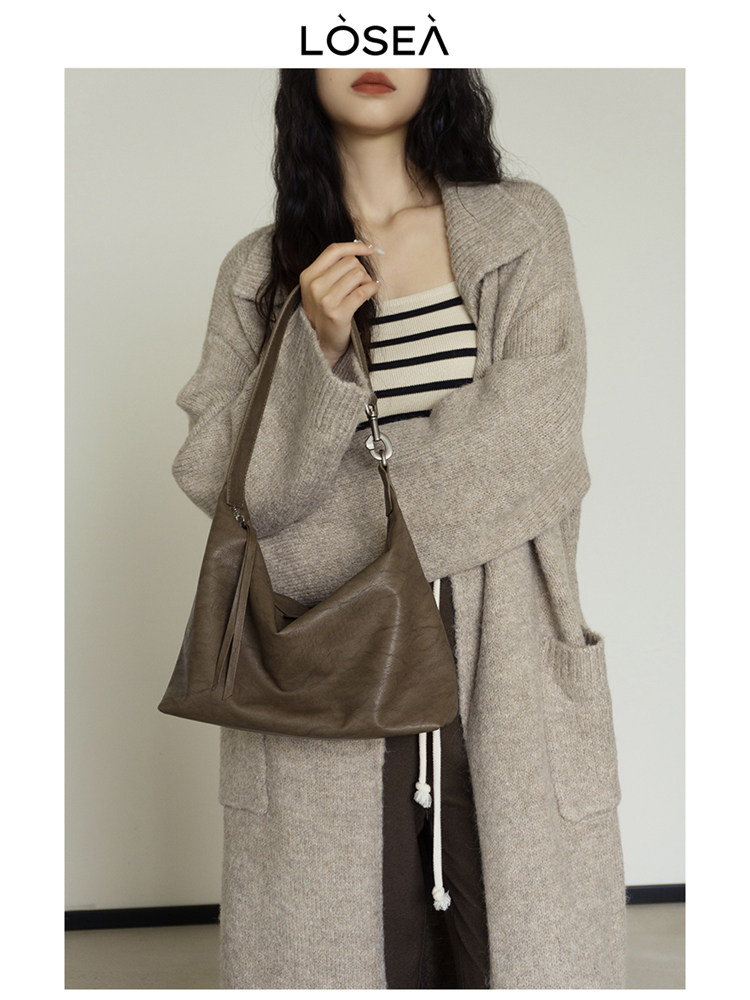 Woman wearing a beige knit cardigan and holding a brown leather shoulder bag