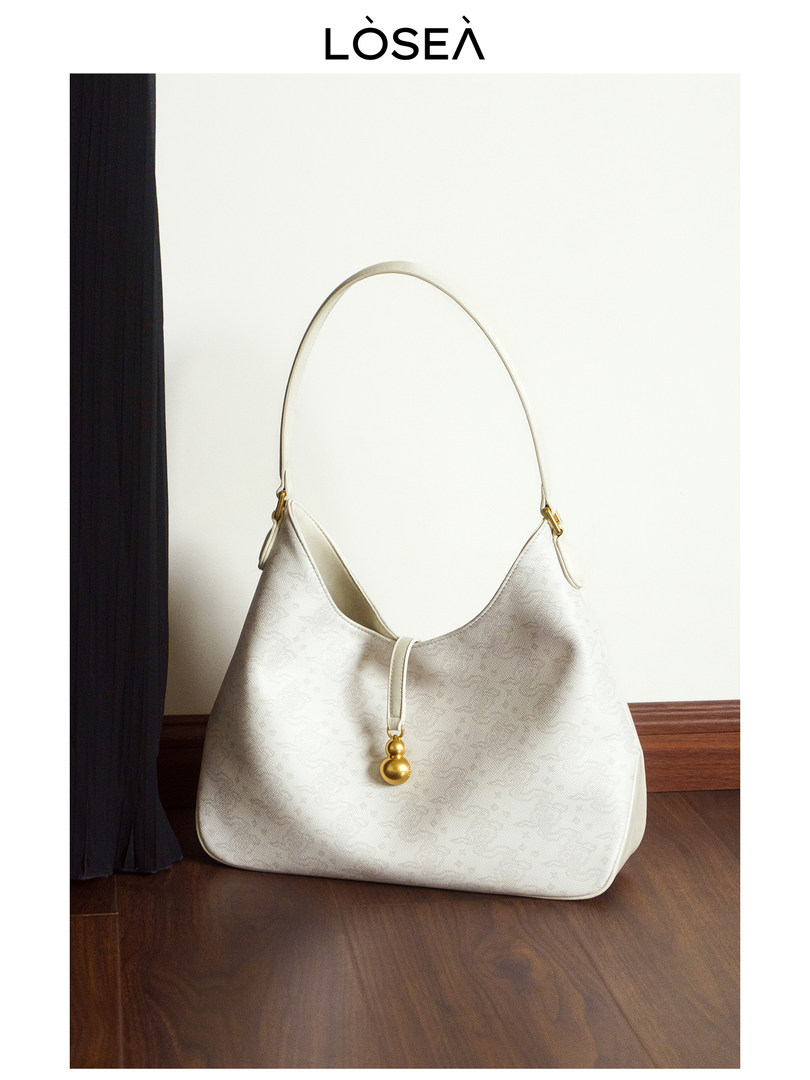 White shoulder handbag with gold charm on a wooden floor