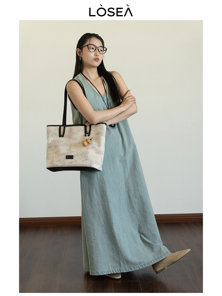 Woman modeling a light blue sleeveless maxi dress with a beige tote bag
