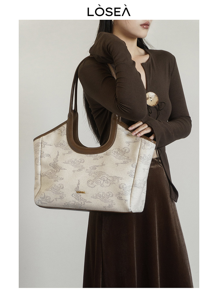 Woman holding a beige patterned tote handbag with brown trim