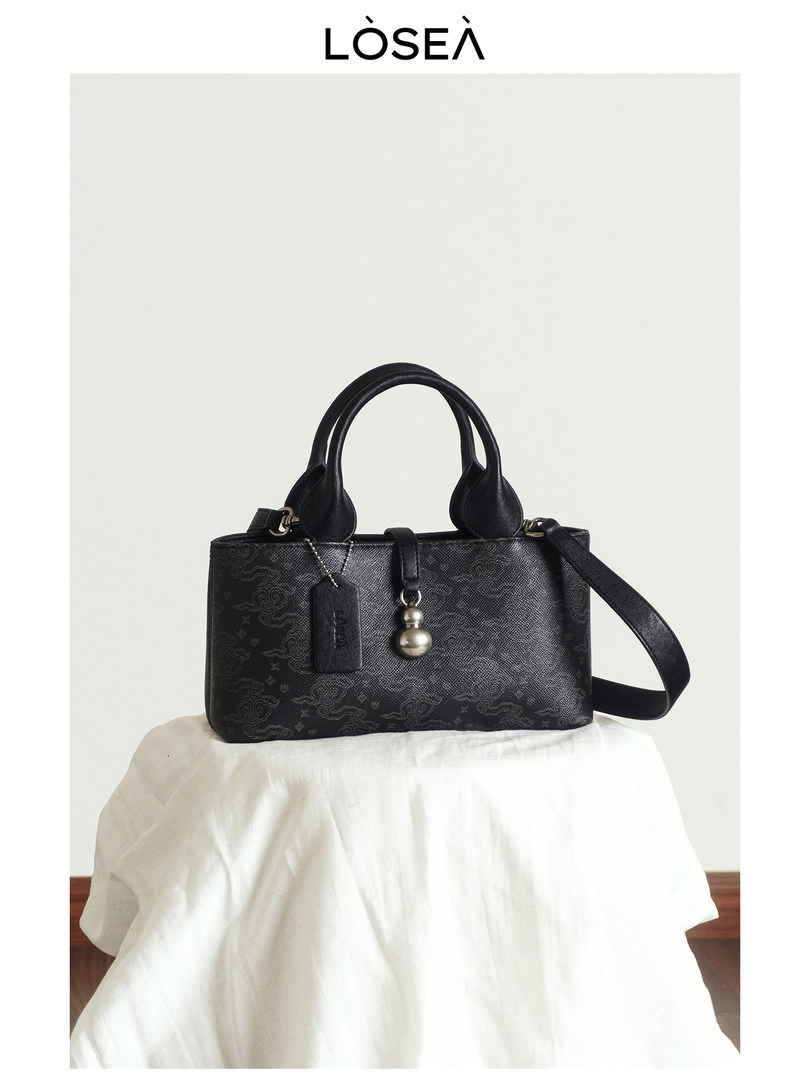 Black leather handbag with top handles and shoulder strap on a white backdrop