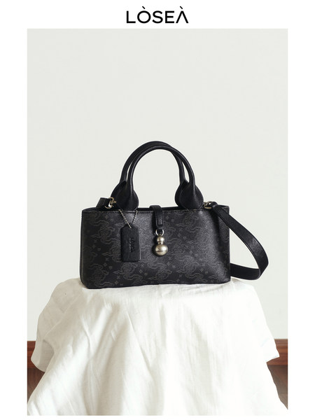 Black leather handbag with top handles and shoulder strap on a white backdrop