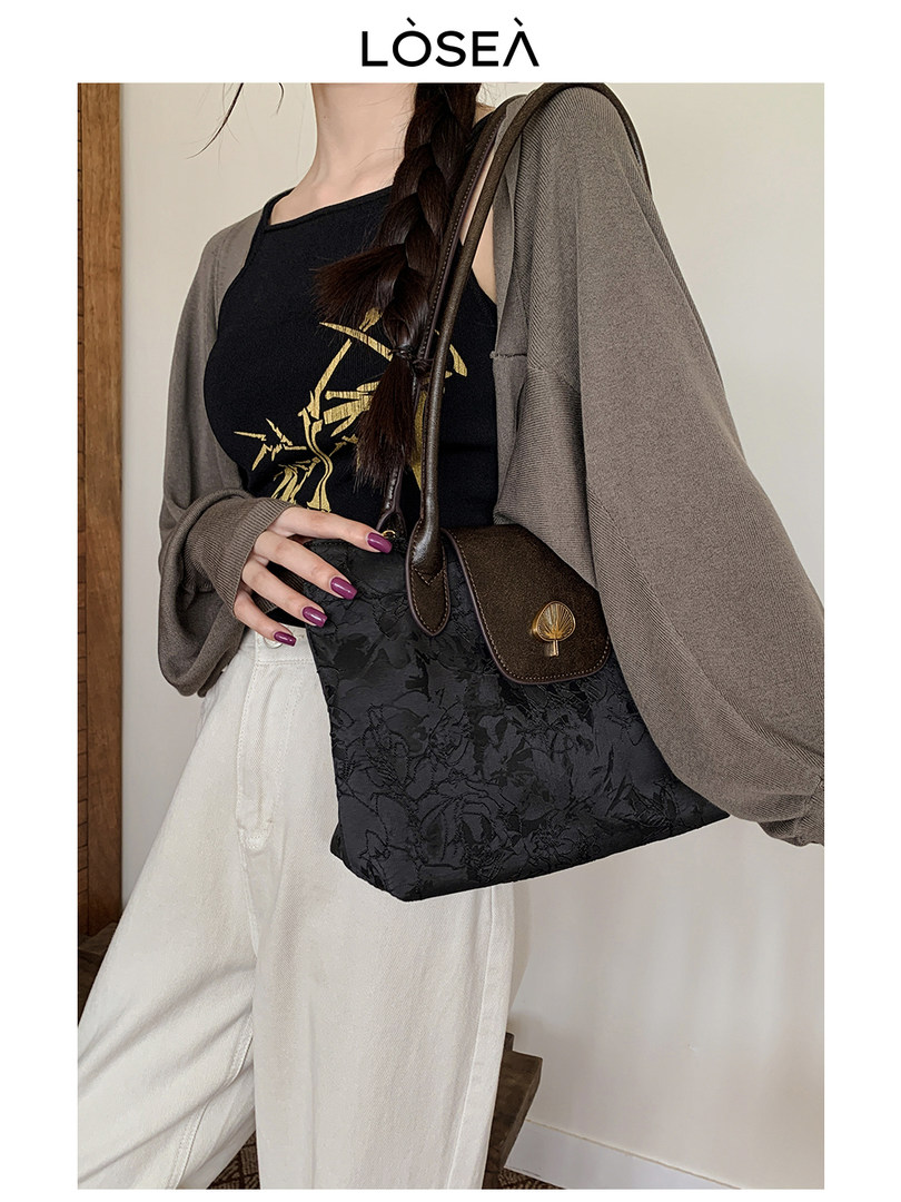 Model wearing a black textured shoulder handbag with brown trim