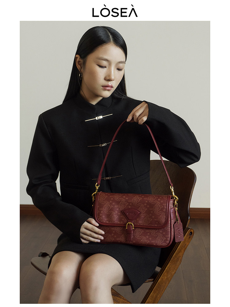 Model holding a burgundy patterned leather handbag while seated