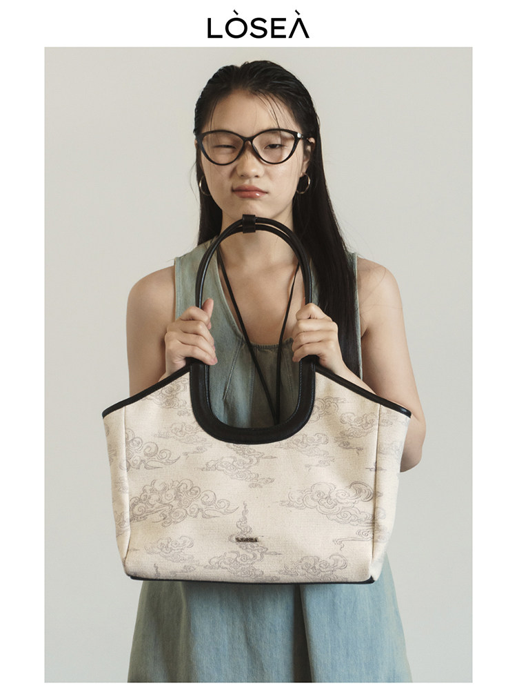 Model holding a beige patterned tote bag with black handles