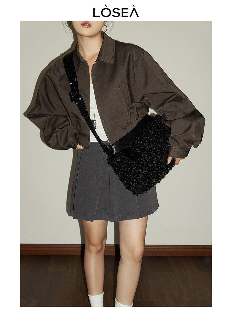 Model wearing a brown cropped jacket with a dark mini skirt and black shoulder bag