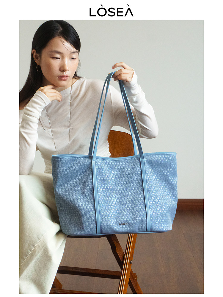 Light blue tote handbag held by a seated model