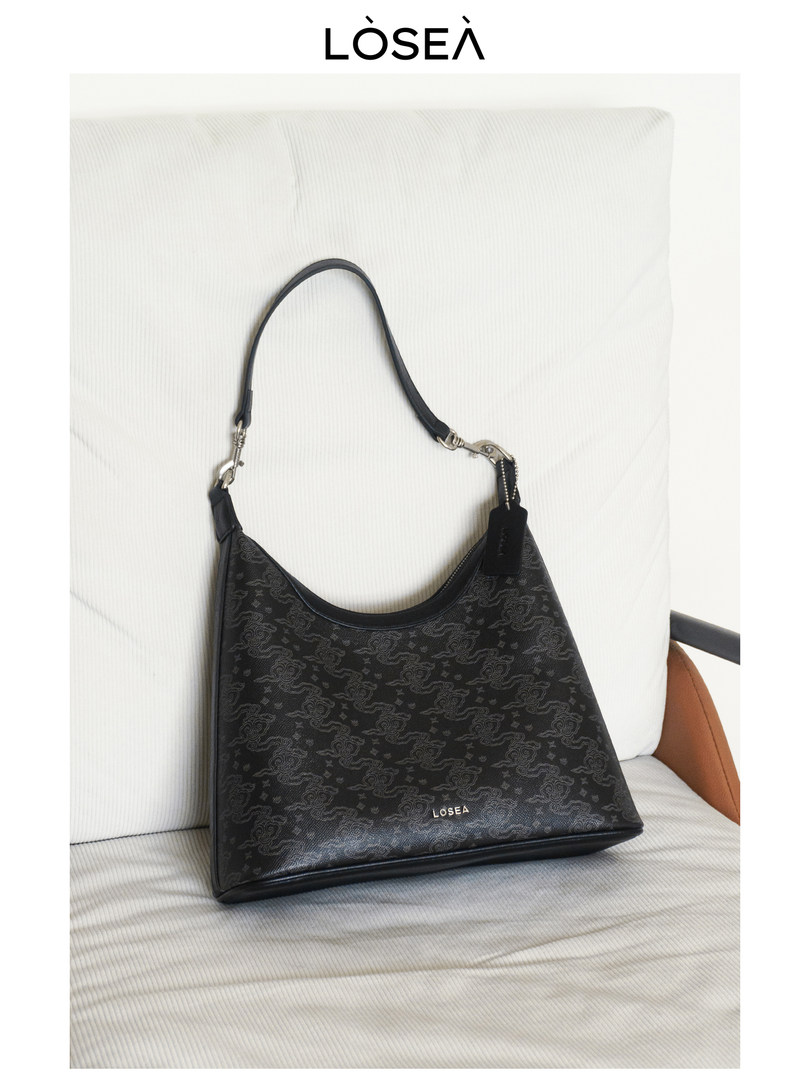 Black patterned shoulder handbag with a strap on a white chair