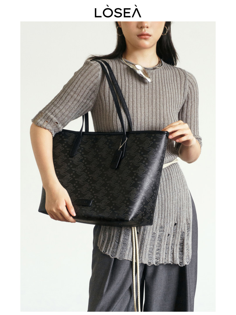 Black patterned tote bag held by a model wearing a gray knit outfit