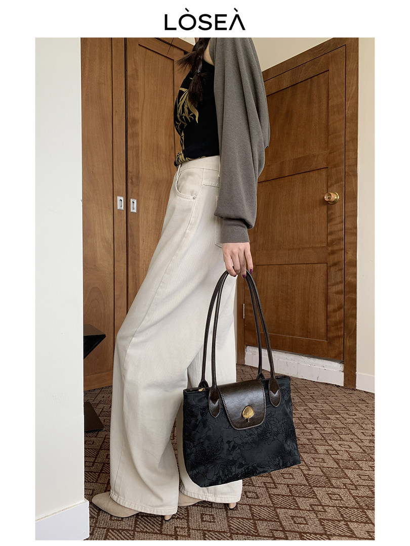 Model holding a black tote handbag while wearing cream wide-leg pants