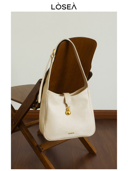 Cream shoulder handbag with gold charm displayed on a chair
