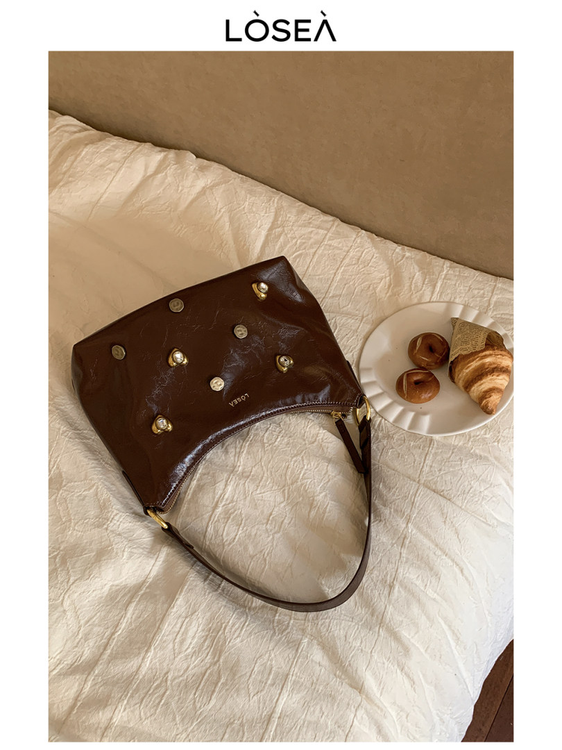 Brown leather handbag with metal studs on a bed