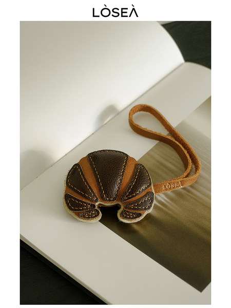 Croissant-shaped leather keychain or charm on a display surface