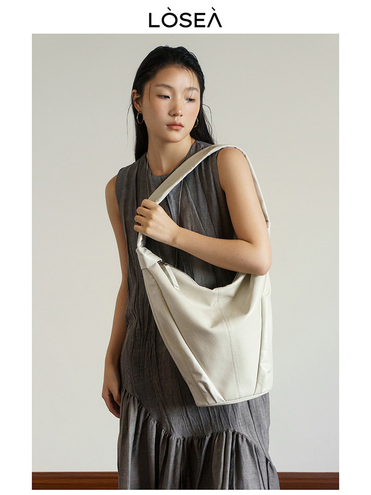Model wearing a cream shoulder bag with a gray dress