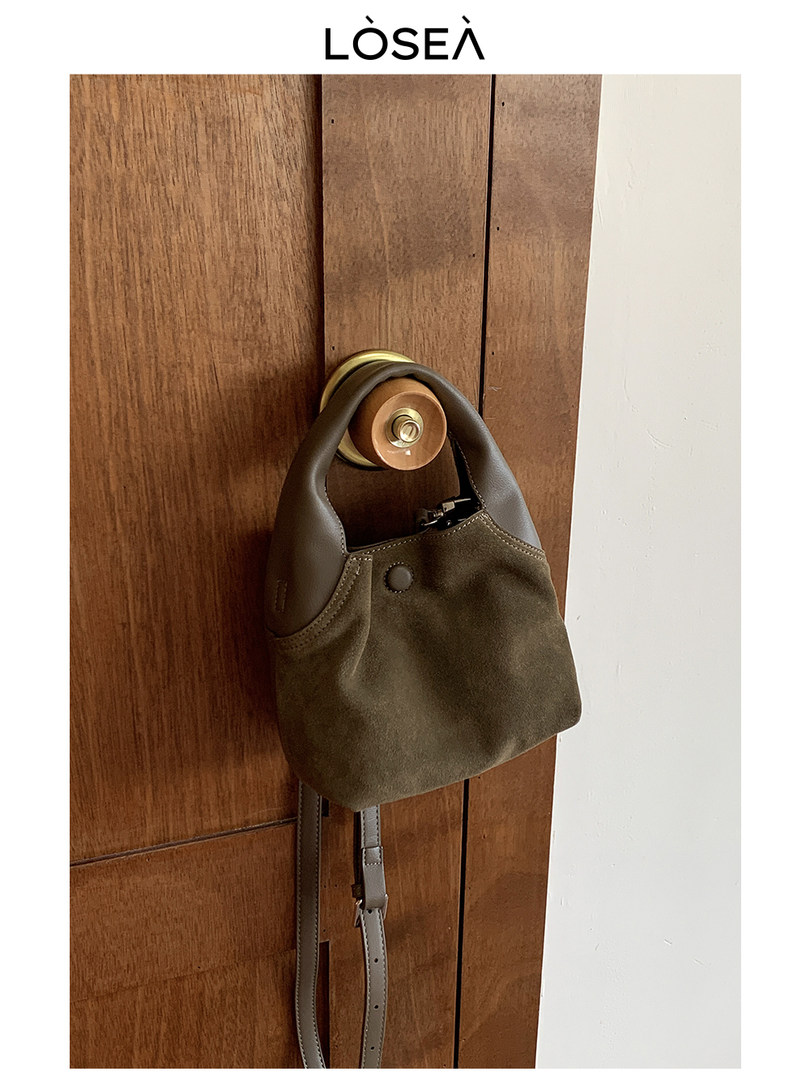 Brown suede and leather shoulder bag hanging on a wooden door