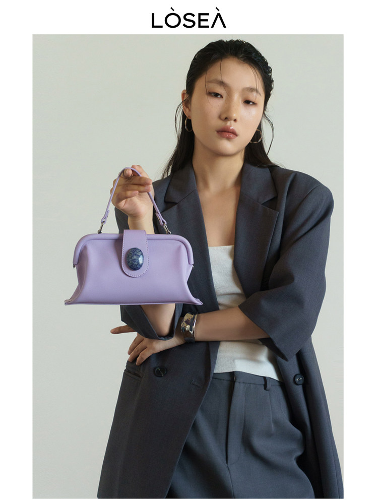 Lavender handbag held by a model in a dark blazer