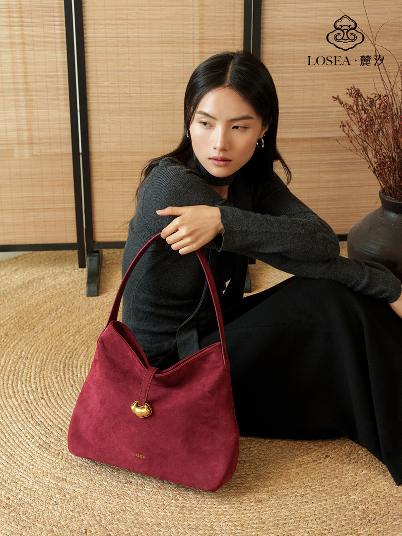 Model holding a burgundy suede shoulder handbag