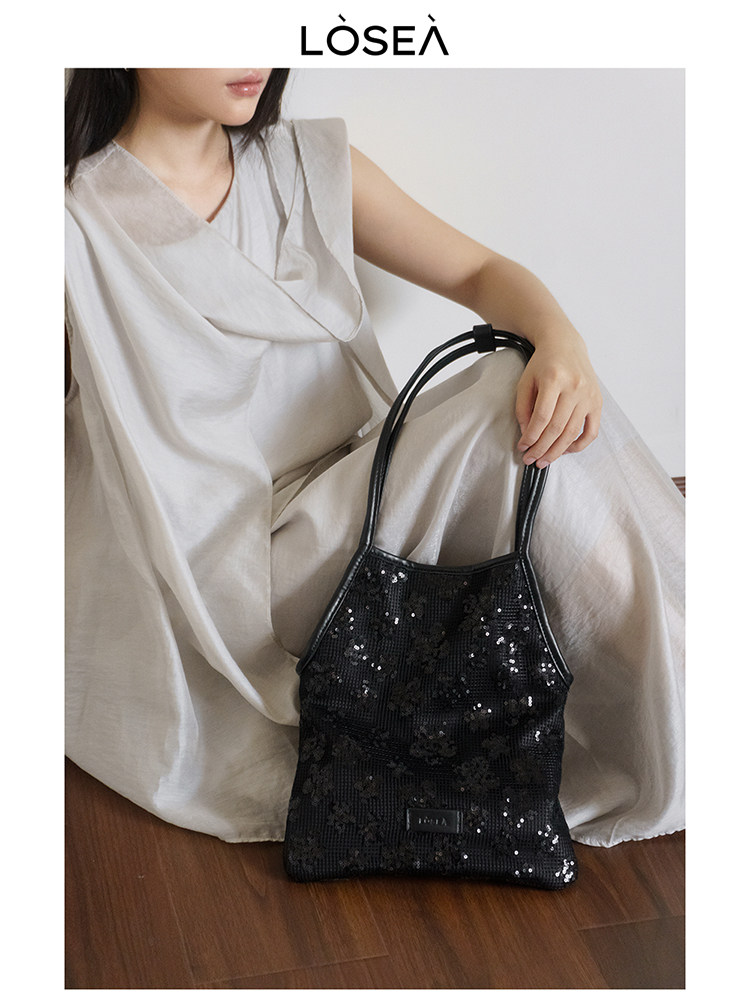 Black sequined shoulder handbag held by a seated model
