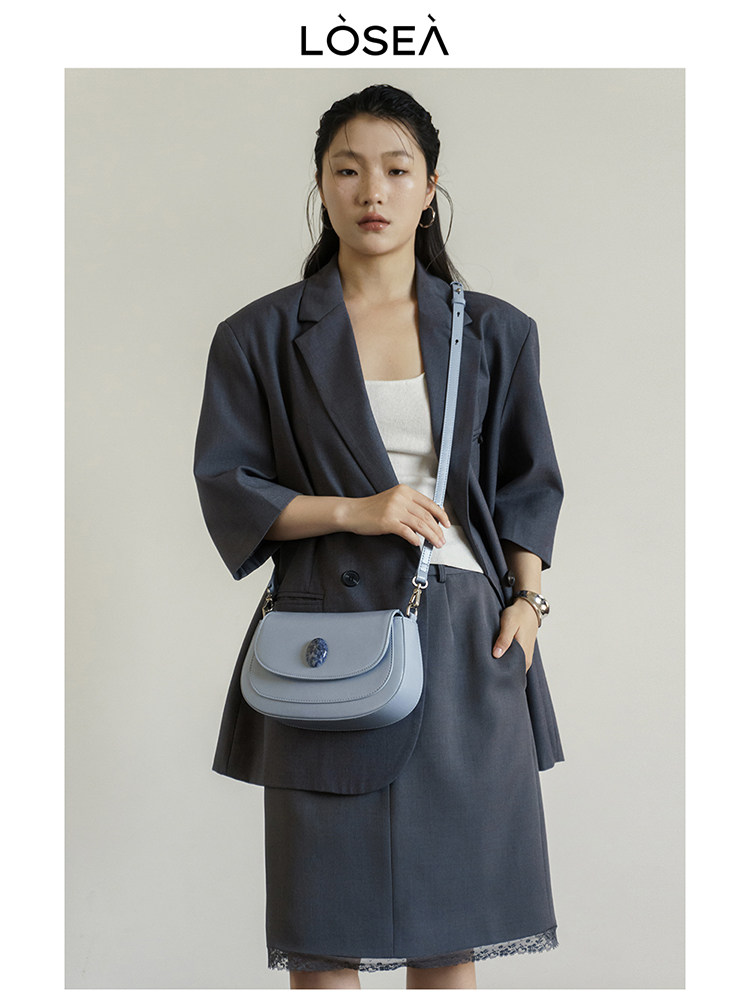 Light blue crossbody handbag worn with a dark blazer and skirt outfit on a model