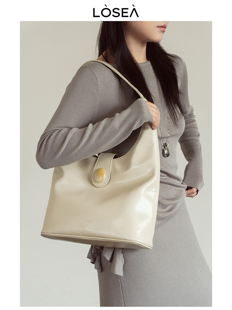 Cream leather shoulder tote bag worn by a model in a neutral knit outfit