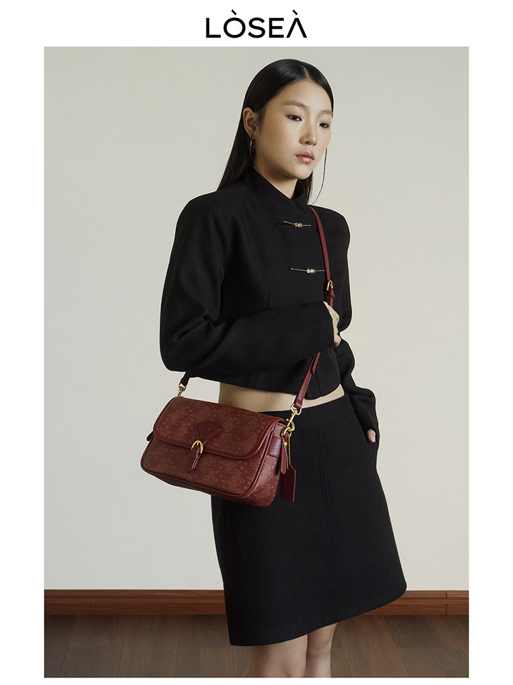 Model wearing a black cropped jacket and skirt with a burgundy shoulder bag