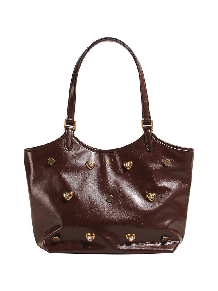 Brown leather shoulder tote bag with decorative heart studs on a white background