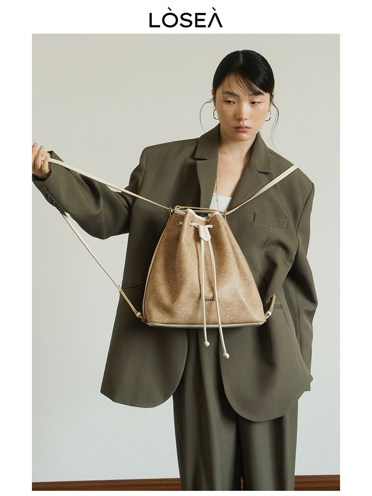 Model wearing an olive suit with a tan drawstring backpack bag