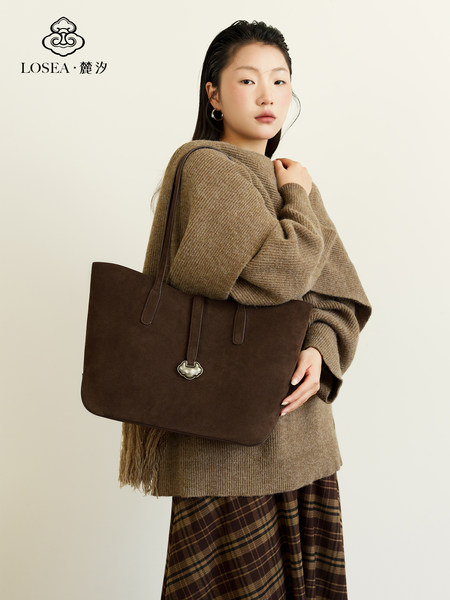 Brown leather tote bag worn by a model with a logo overlay