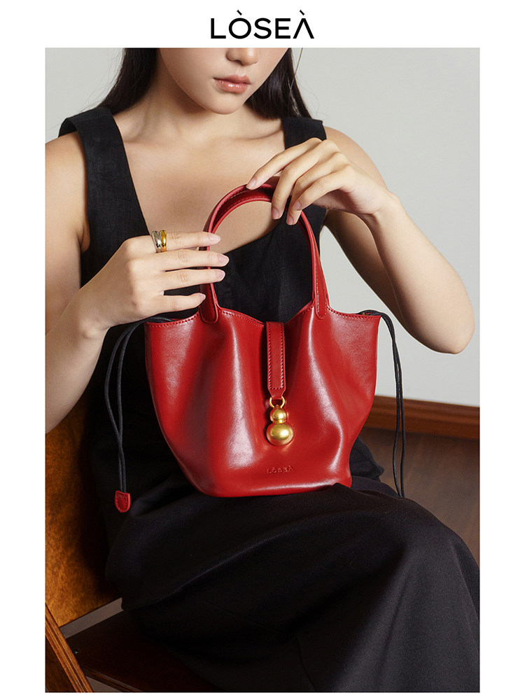 Red leather handbag held by a woman in a black dress