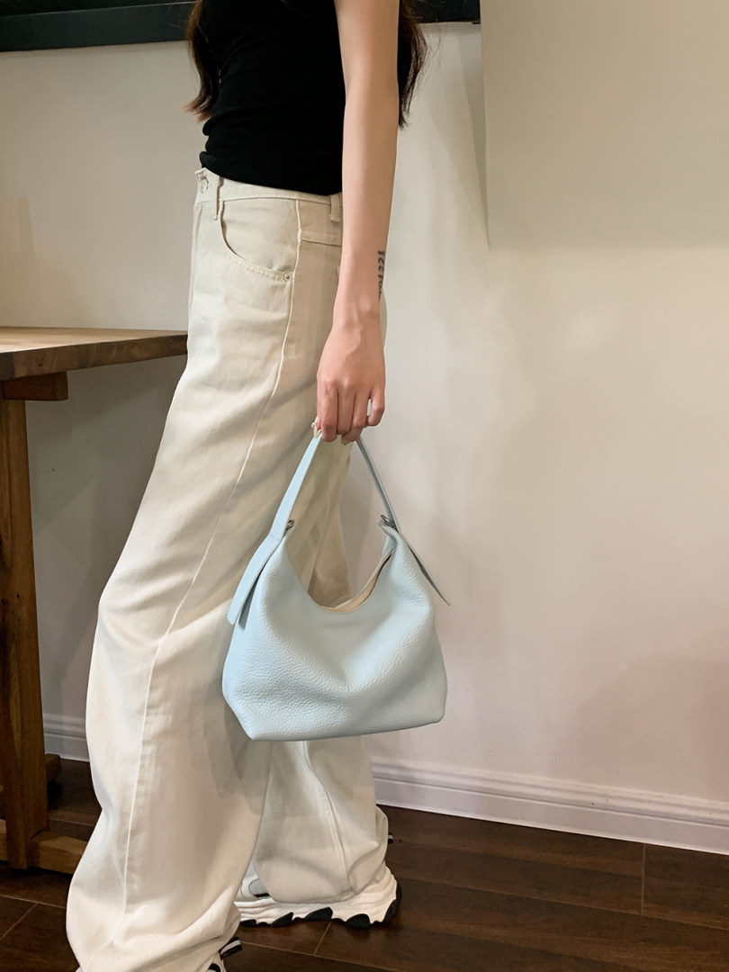 Model wearing cream wide-leg jeans and holding a light blue shoulder bag