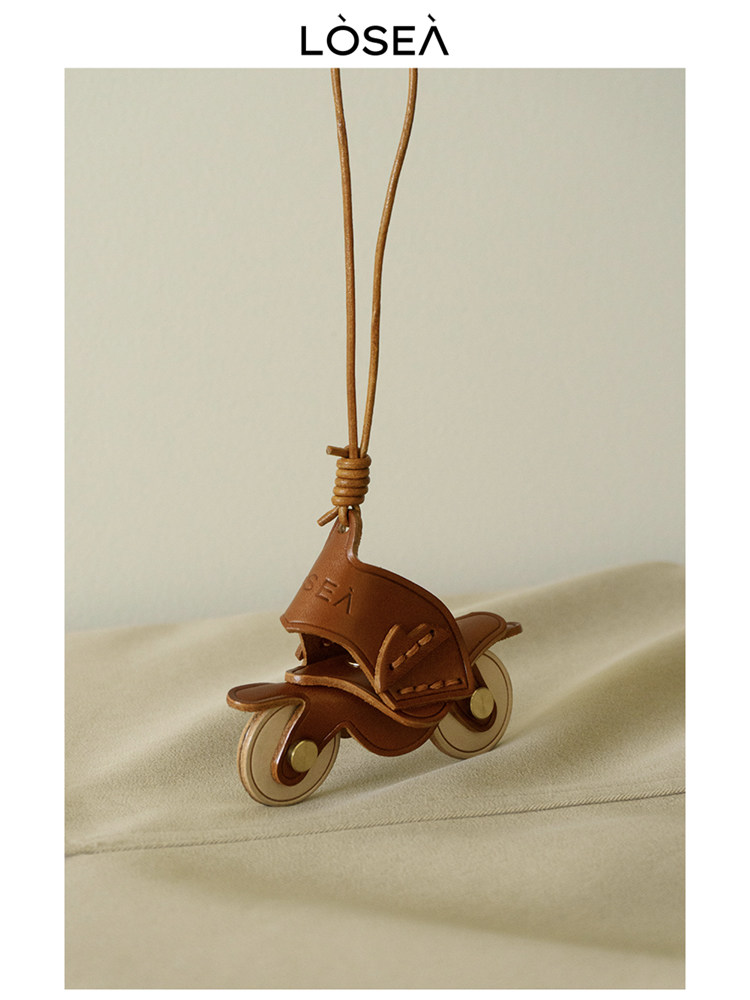 Brown leather scooter pendant necklace on a beige background