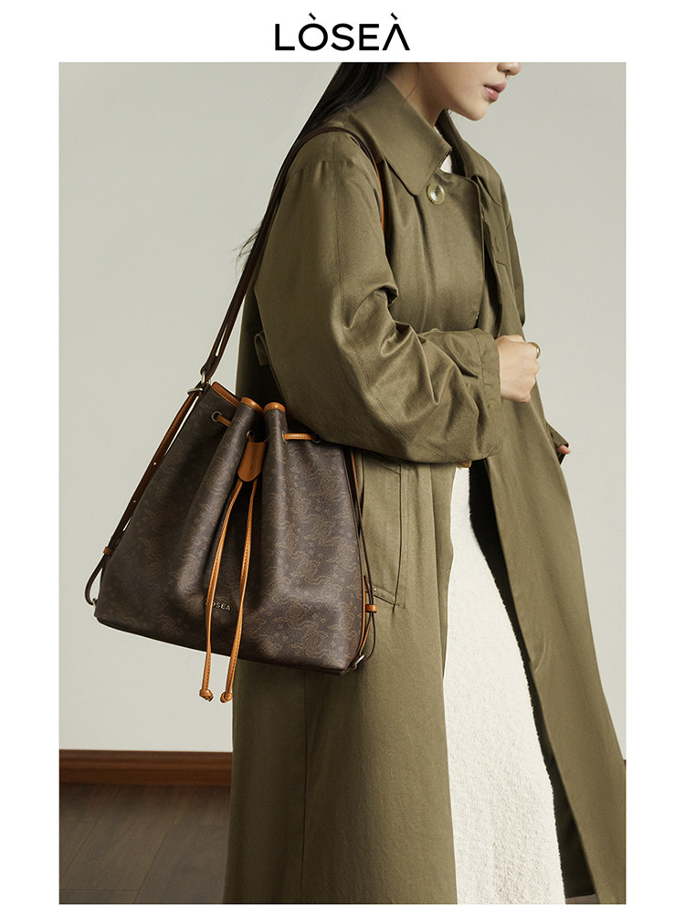 Model wearing an olive coat carrying a brown drawstring shoulder bag