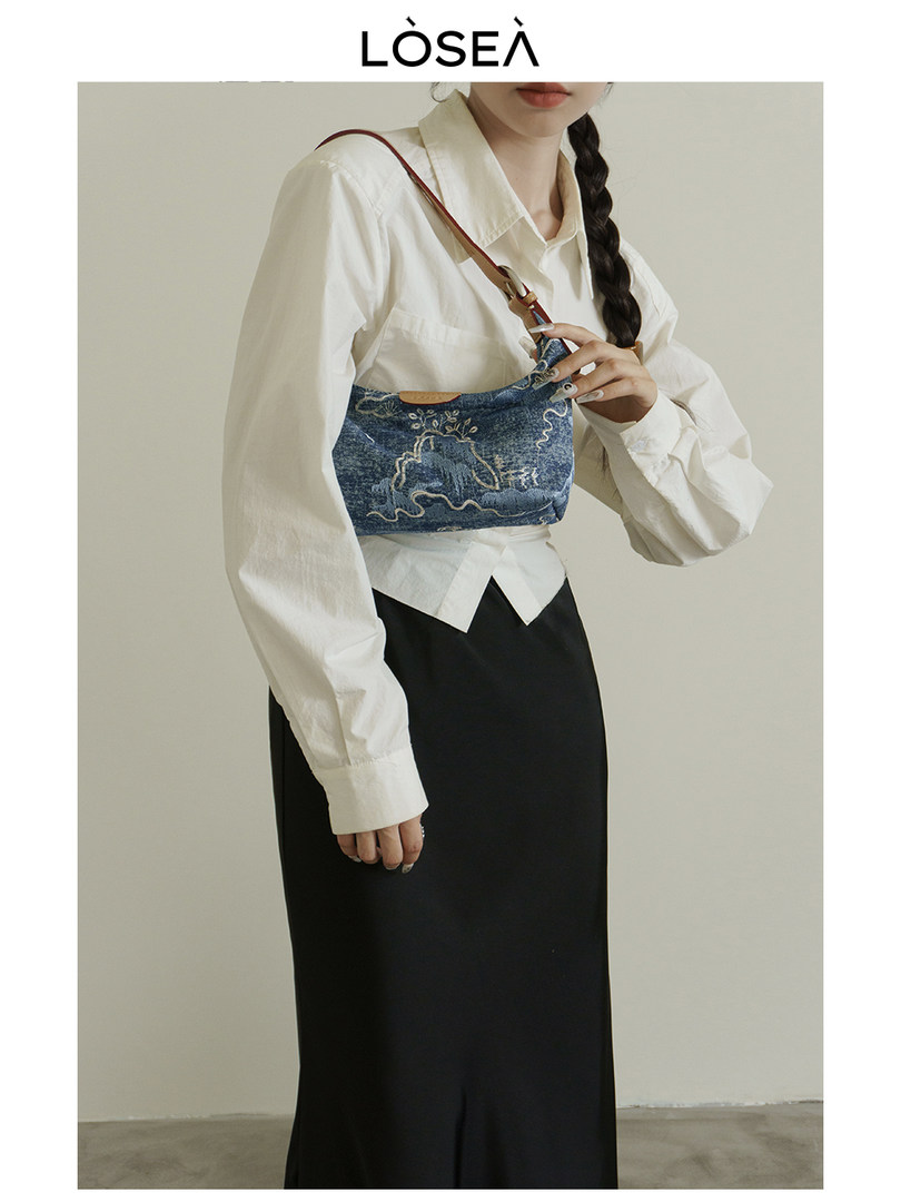 Woman wearing a blue denim shoulder bag over a white shirt and black skirt