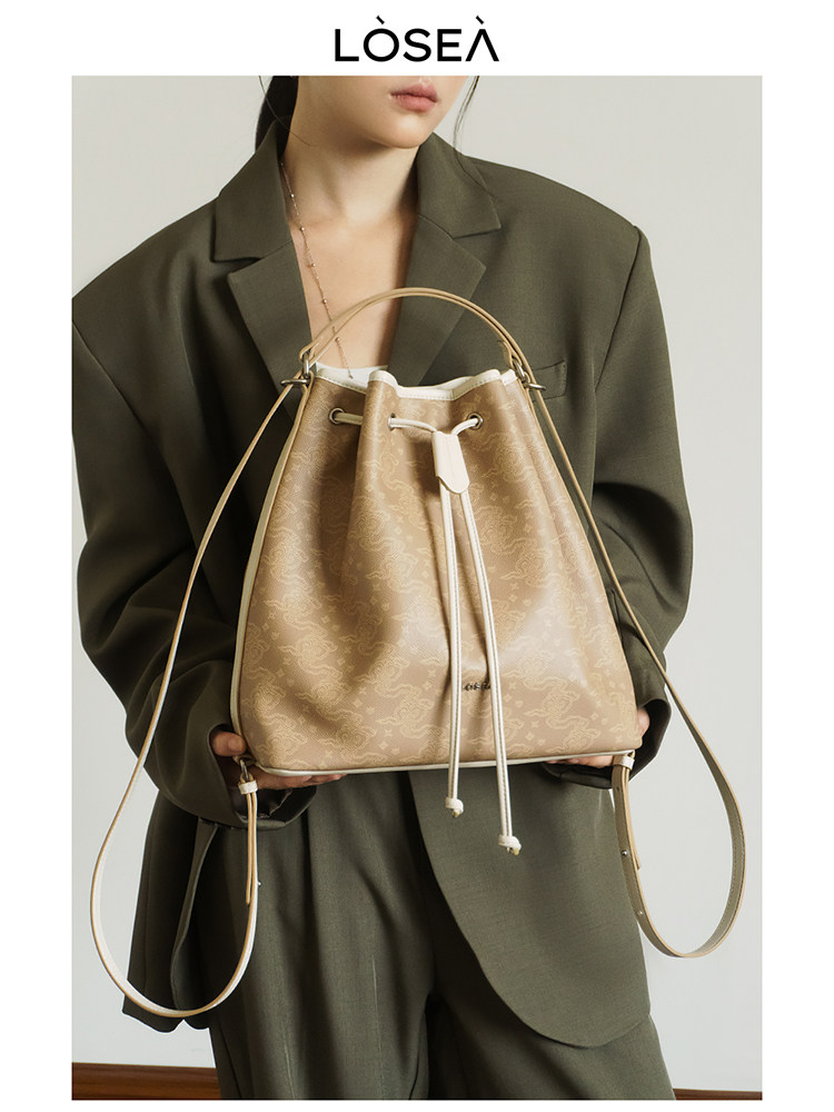 Beige patterned drawstring bucket bag held by a model
