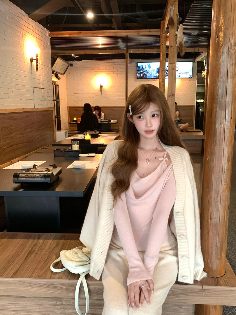 Woman wearing a soft pink layered top with a cream cardigan in a restaurant