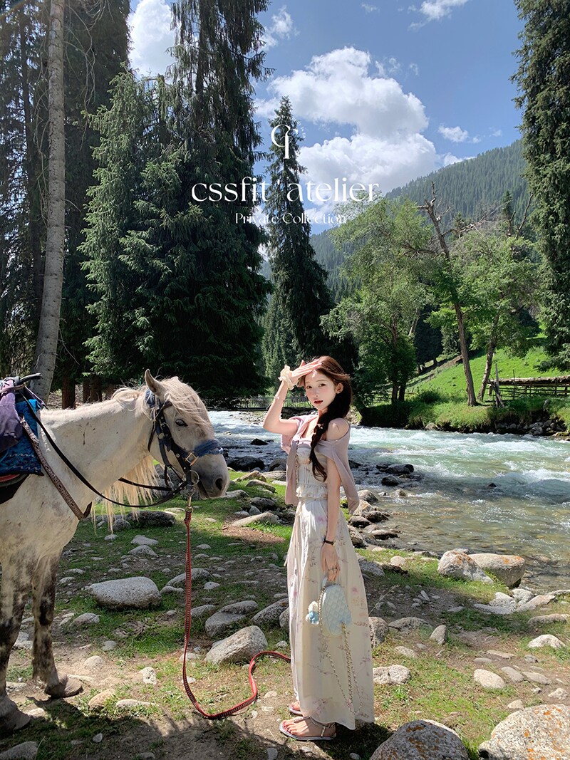 Woman wearing a light-colored dress outdoors by a river with a horse