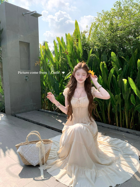 Cream off-shoulder maxi dress worn by a model outdoors with a woven straw bag