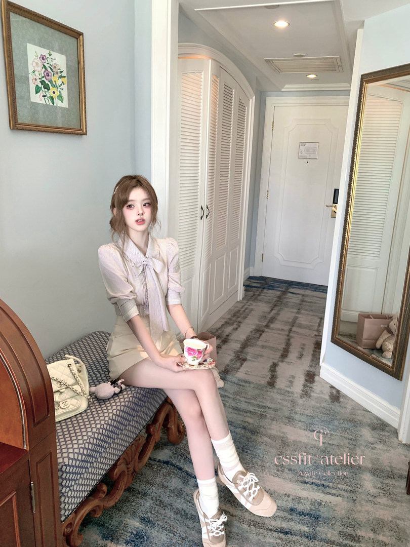 Woman modeling a pastel blouse and skirt outfit seated indoors