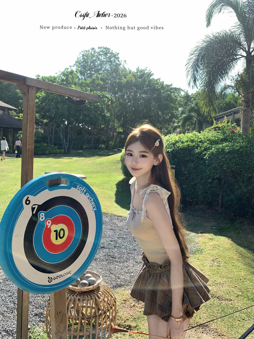 Model wearing a beige knit top with a plaid pleated skirt outdoors