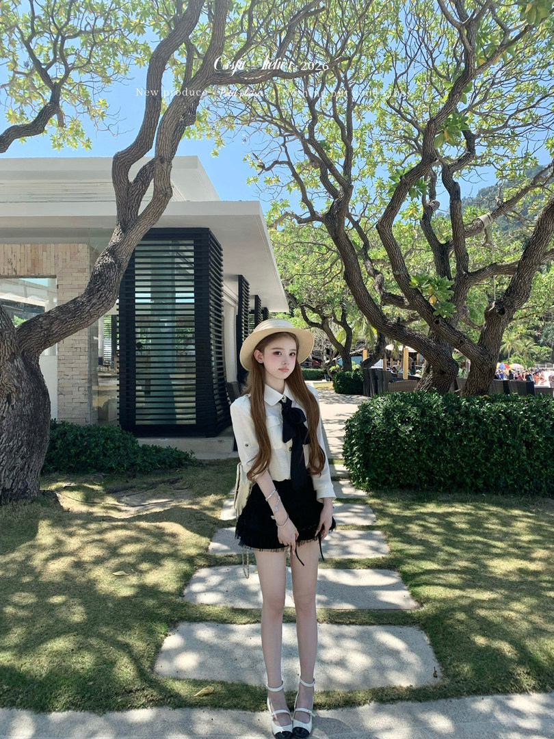 Woman wearing a white blouse, black mini skirt, straw hat, and white heels outdoors