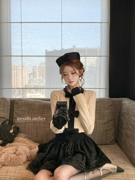 Woman modeling a cream-and-black elegant outfit while seated on a sofa