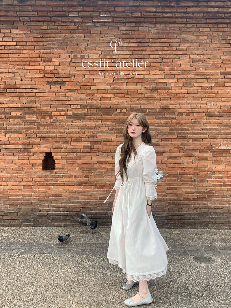Woman wearing a long white dress with lace details against a brick wall