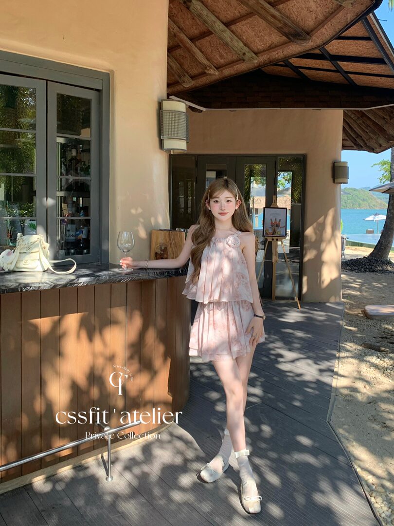 Woman wearing a light pink floral two-piece dress at a seaside resort